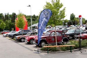 Parkplatz mit historischen Autos, einem Kiwani-Flaggenbanner und einer Sitzecke unter Bäumen.