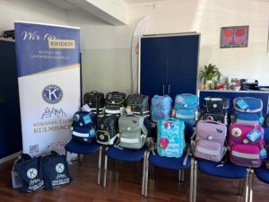 Diverse Schulranzen stehen auf blauen Stühlen, daneben ein Banner des Kiwanis Clubs Kulmbach mit der Aufschrift "Wir für Kinder!".