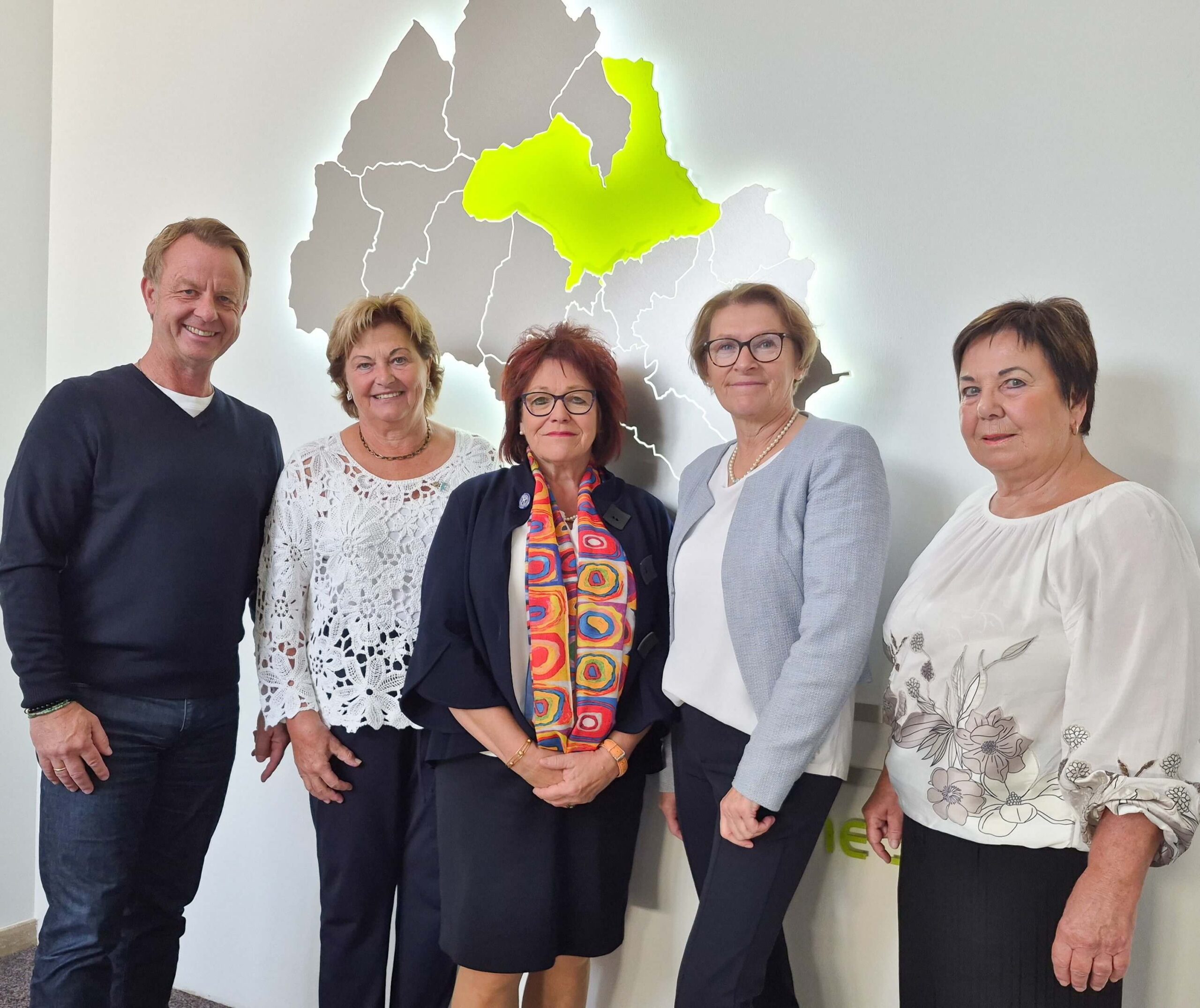 Fünf Personen in formeller Kleidung stehen vor einer beleuchteten Landkarte mit einer hervorgehobenen Region.