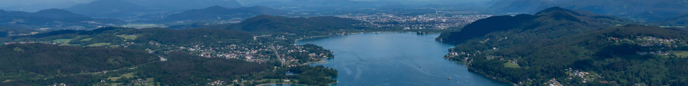 Landschaft mit einem See, umgeben von Hügeln und Bergen, unter einem klaren blauen Himmel.