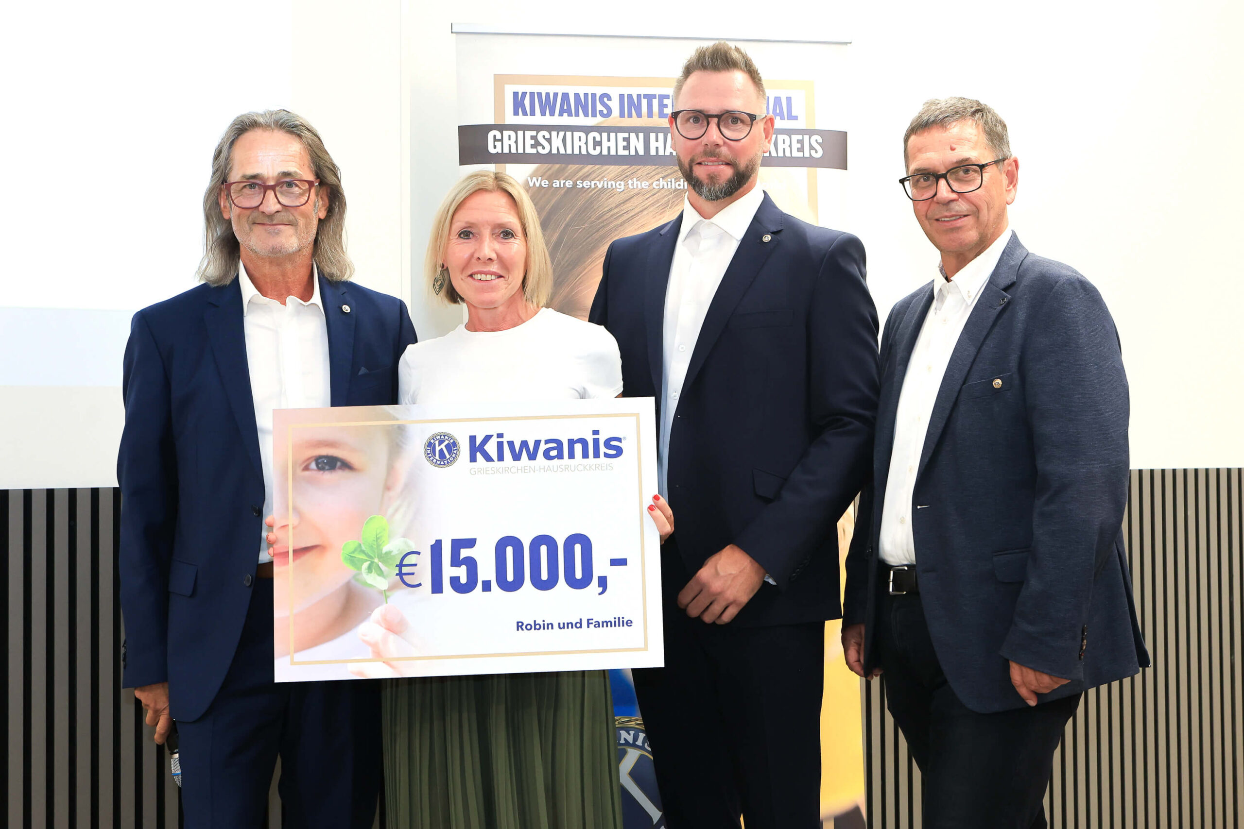 Vier Personen stehen zusammen und halten ein Schild mit einem Scheck über 15.000 Euro für Robin und Familie.