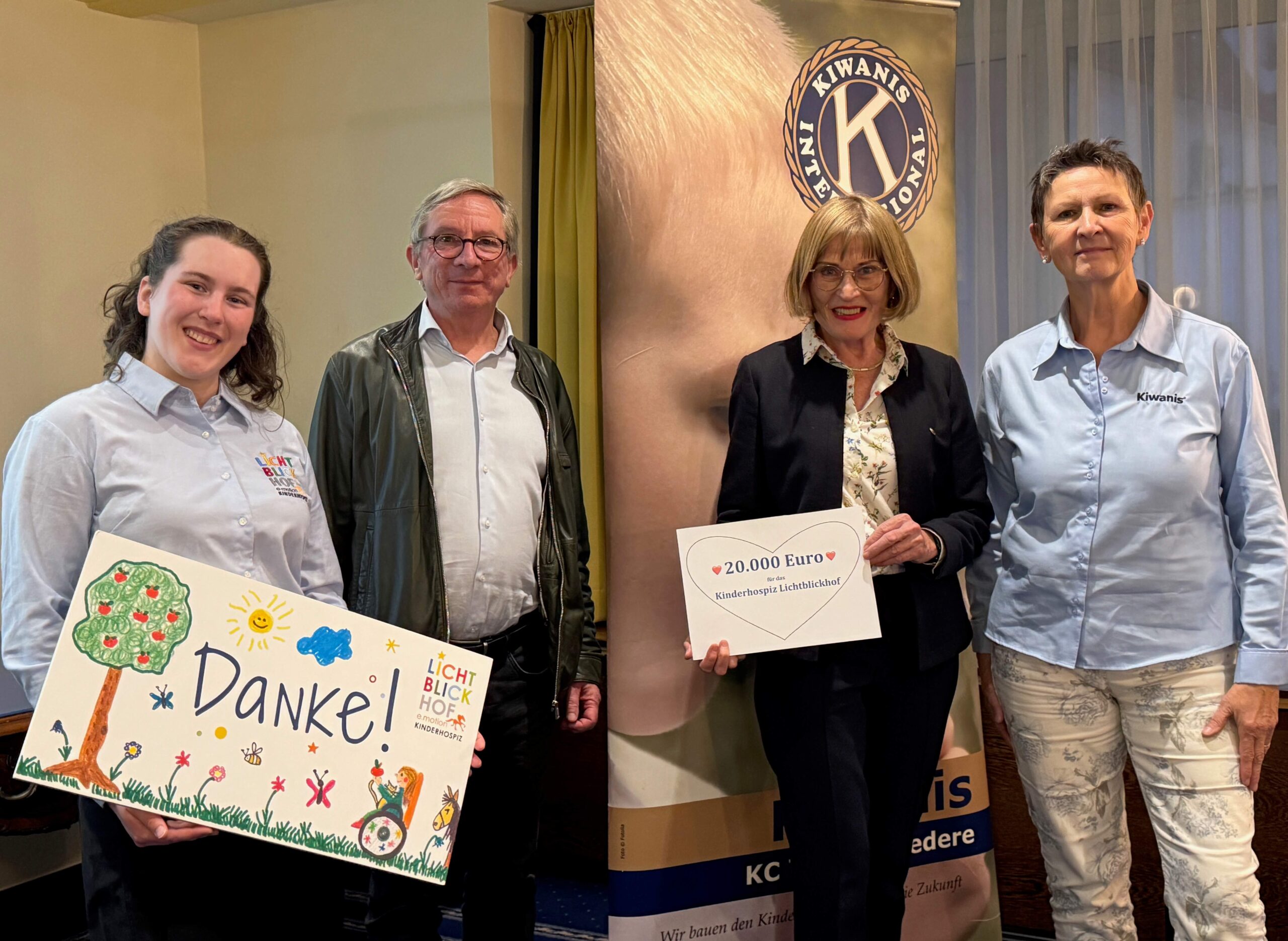 Vier Personen stehen lächelnd zusammen, eine hält ein Dankesschild, die anderen präsentieren einen Scheck über 20.000 Euro für ein Kinderhospiz.